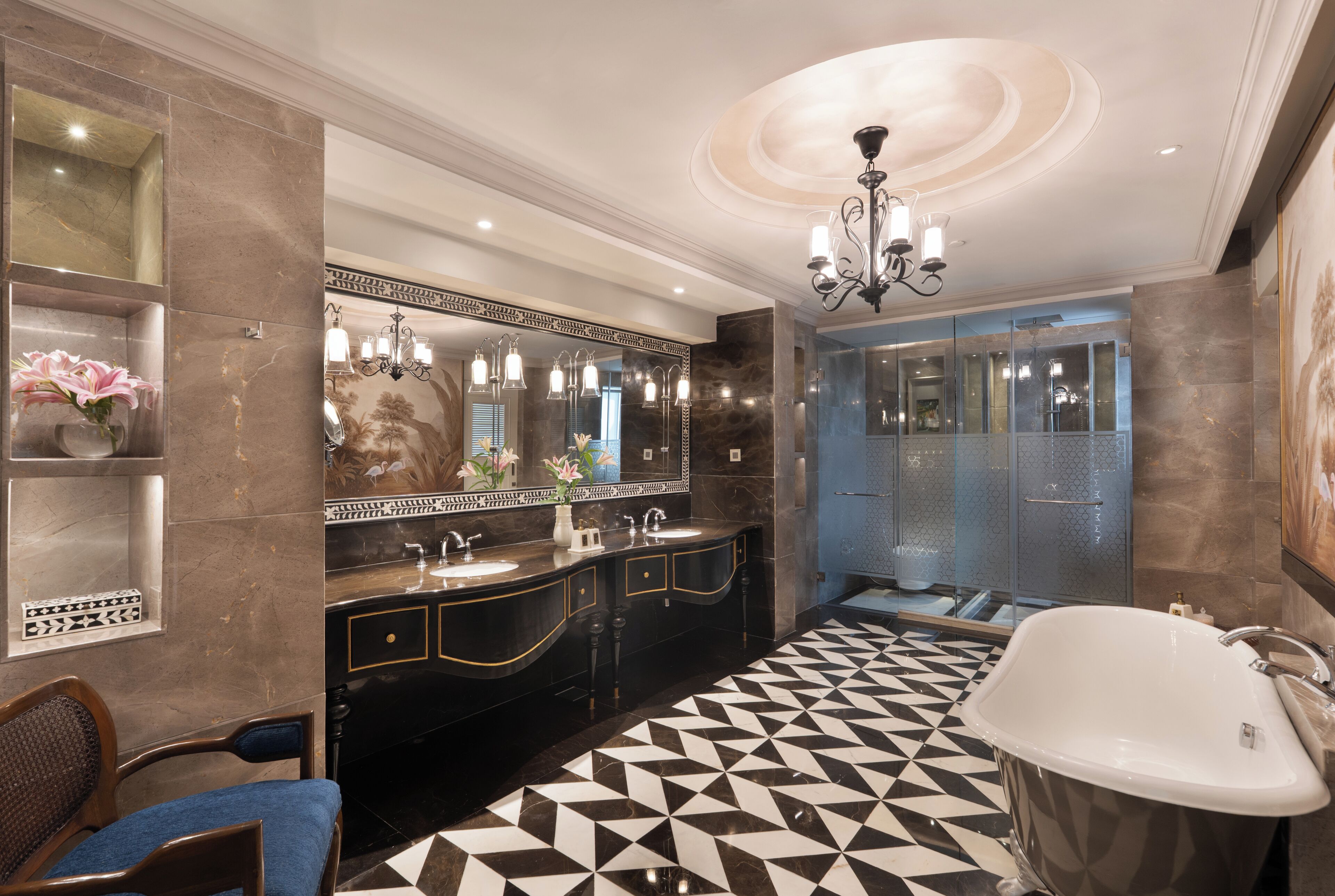 A luxurious bathroom with a large mirror, black and white tiled floor, a freestanding bathtub, and a chandelier.