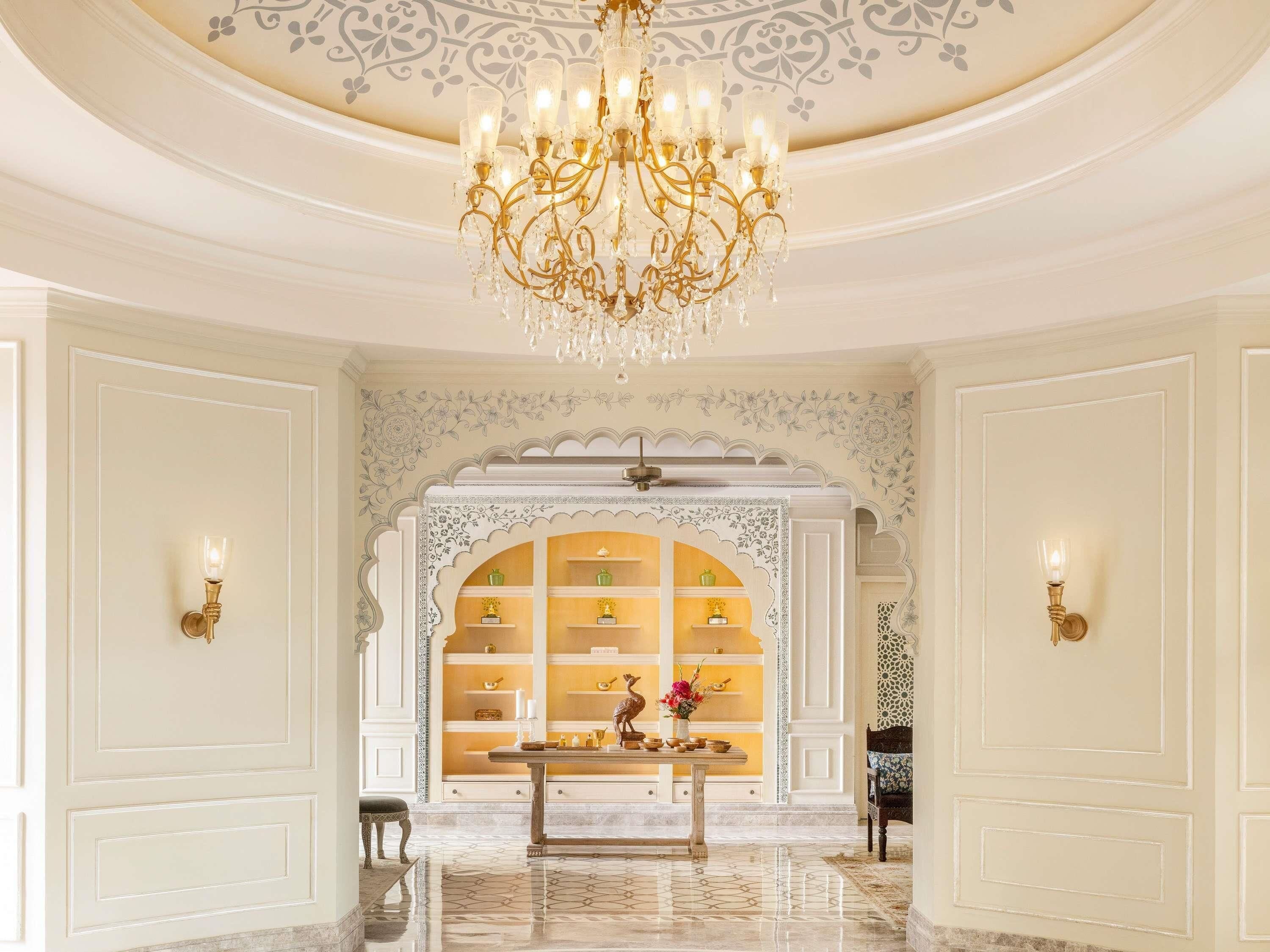 A grand hallway with a chandelier, ornate wall decorations, and a display cabinet with items.