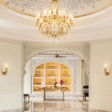 A grand hallway with a chandelier, ornate wall decorations, and a display cabinet with items.