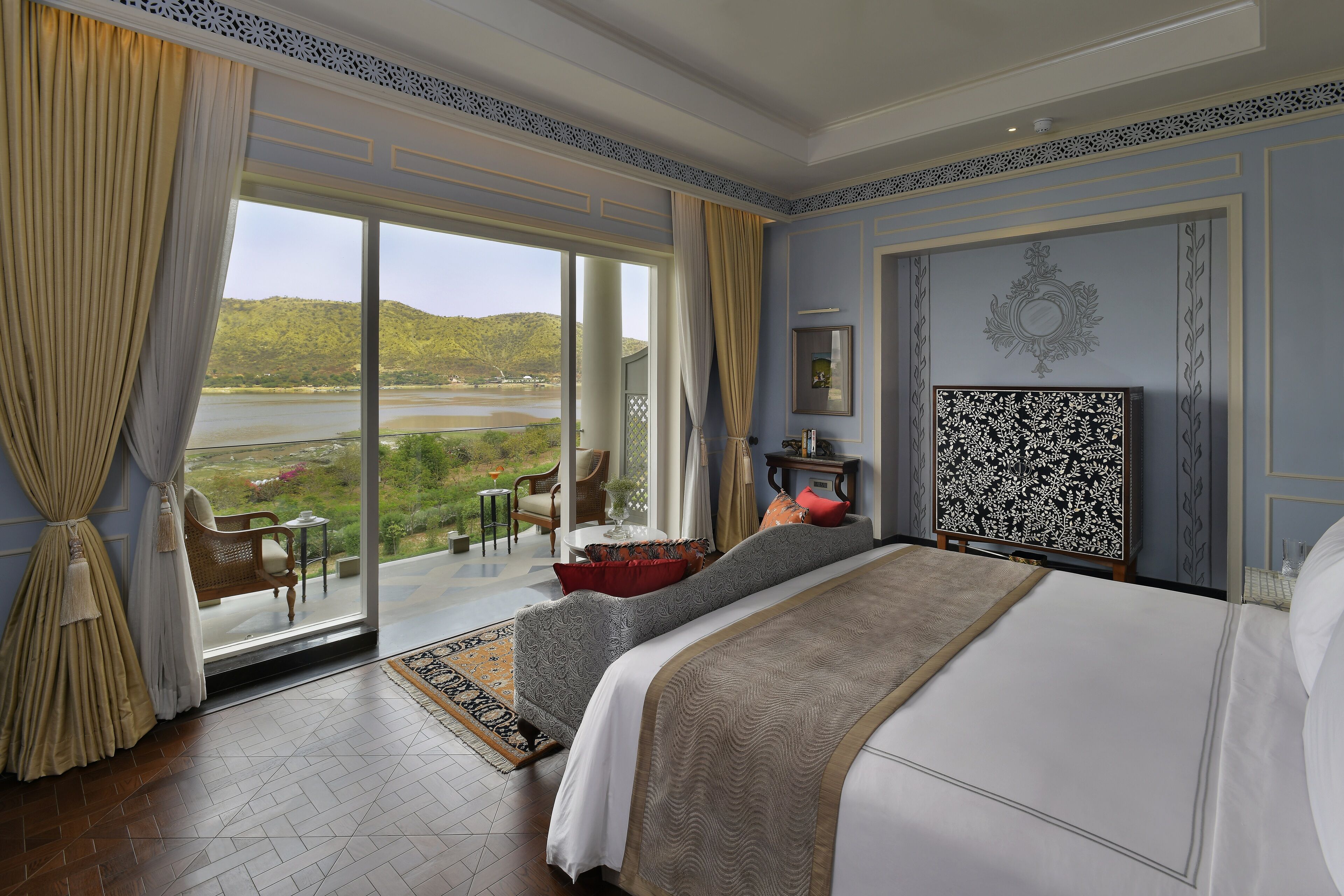 Una camera da letto con un letto grande, vista su un lago e un balcone con mobili da esterno.