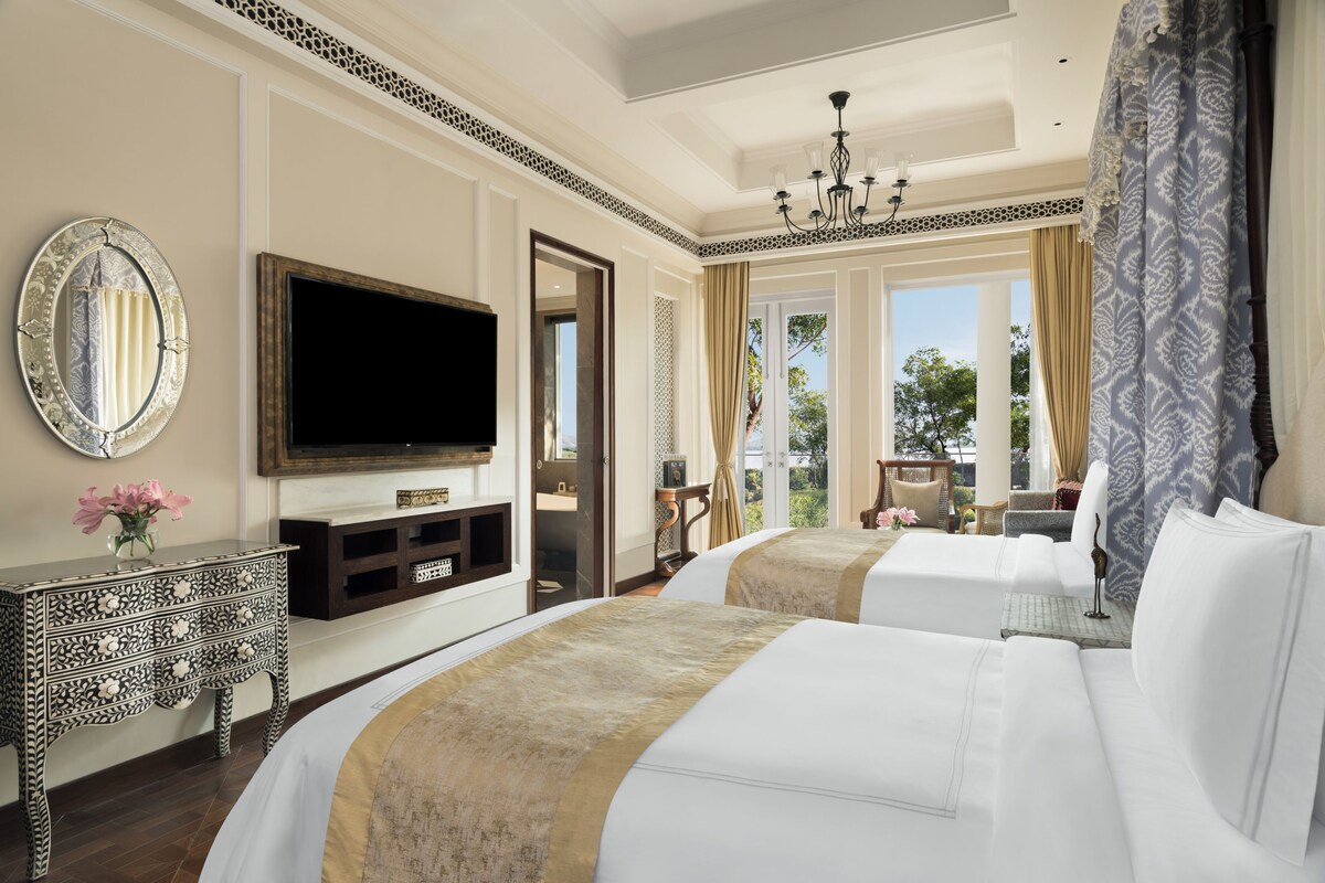 A hotel room with two beds, a television, a decorative mirror, and a view of the outdoors.
