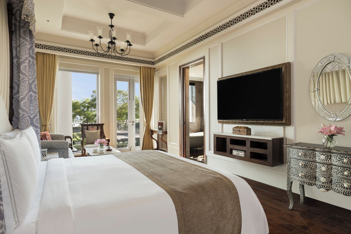 A large bed with a headboard, a television mounted on the wall, a decorative console table, and a view of the outdoors.