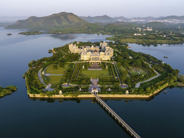 A large, luxurious estate with a central building, surrounded by water and greenery, connected by a bridge.