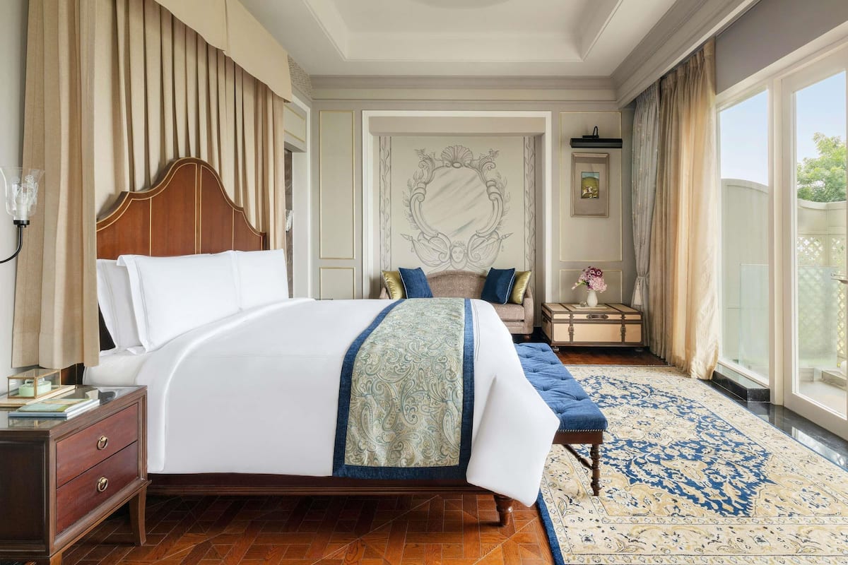 A hotel room with a large bed, a wooden nightstand, a small table with a vase, a sofa, and a large window with a view.