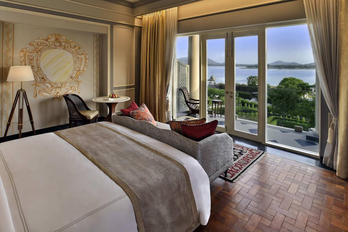 A hotel room with a large bed, a small table with fruit, a chair, and a view of a lake.