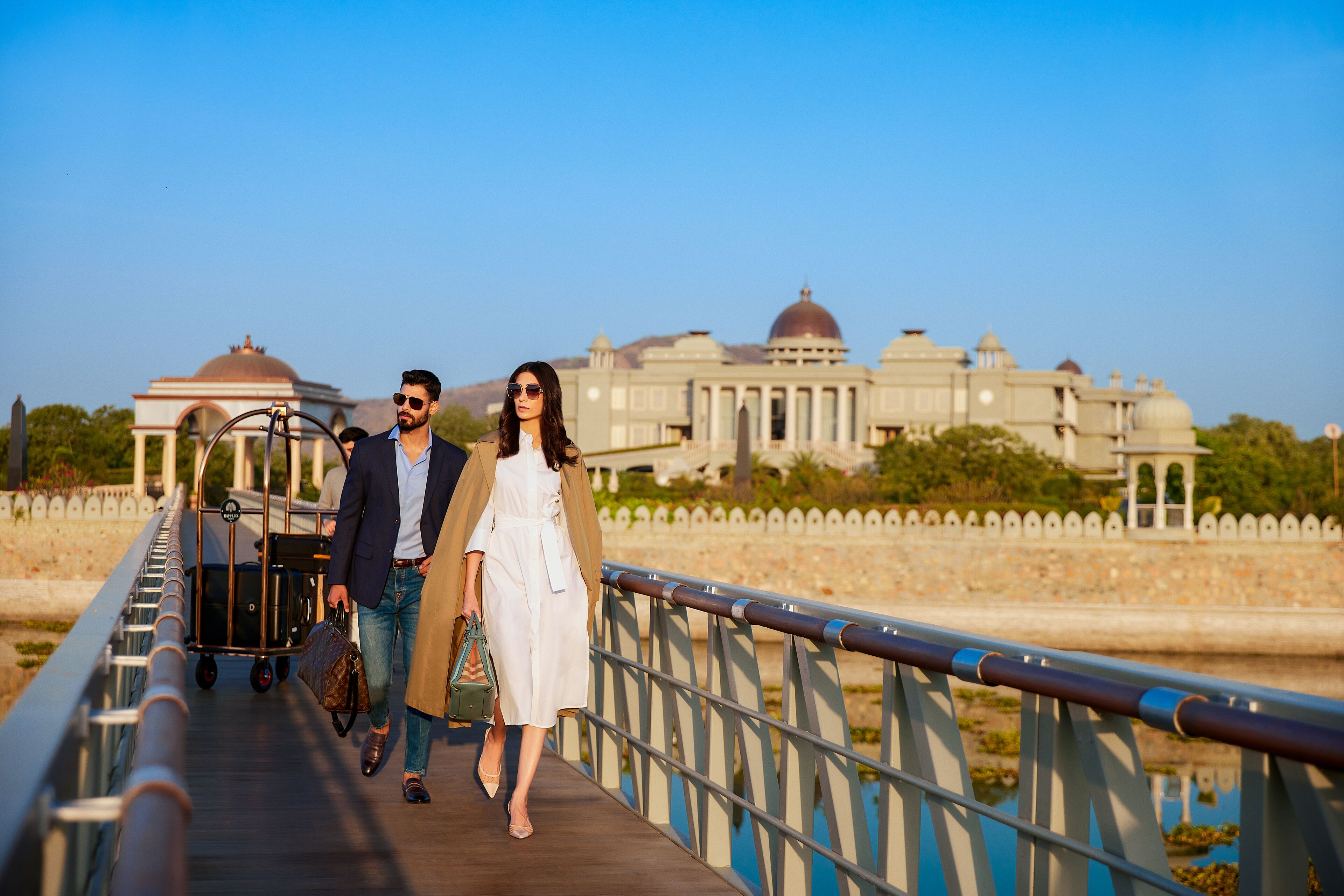 A couple walking on a bridge with a historic building in the background.