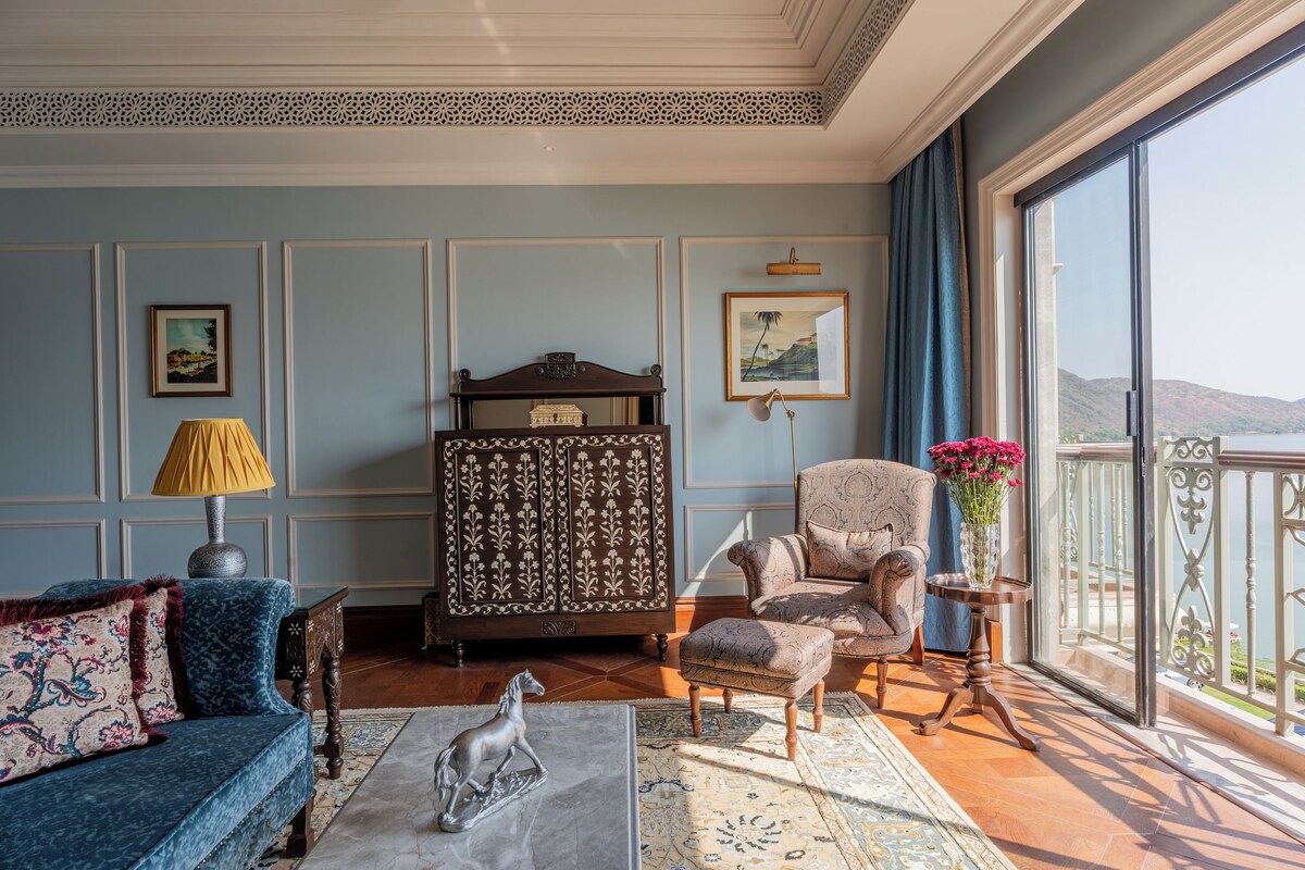 A room with a blue wall, a sofa, a chair, a cabinet, and a balcony with a view.