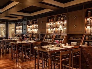 A restaurant with wooden tables and chairs, shelves with jars, and a warm ambiance. - Raffles Udaipur (Udaipur)