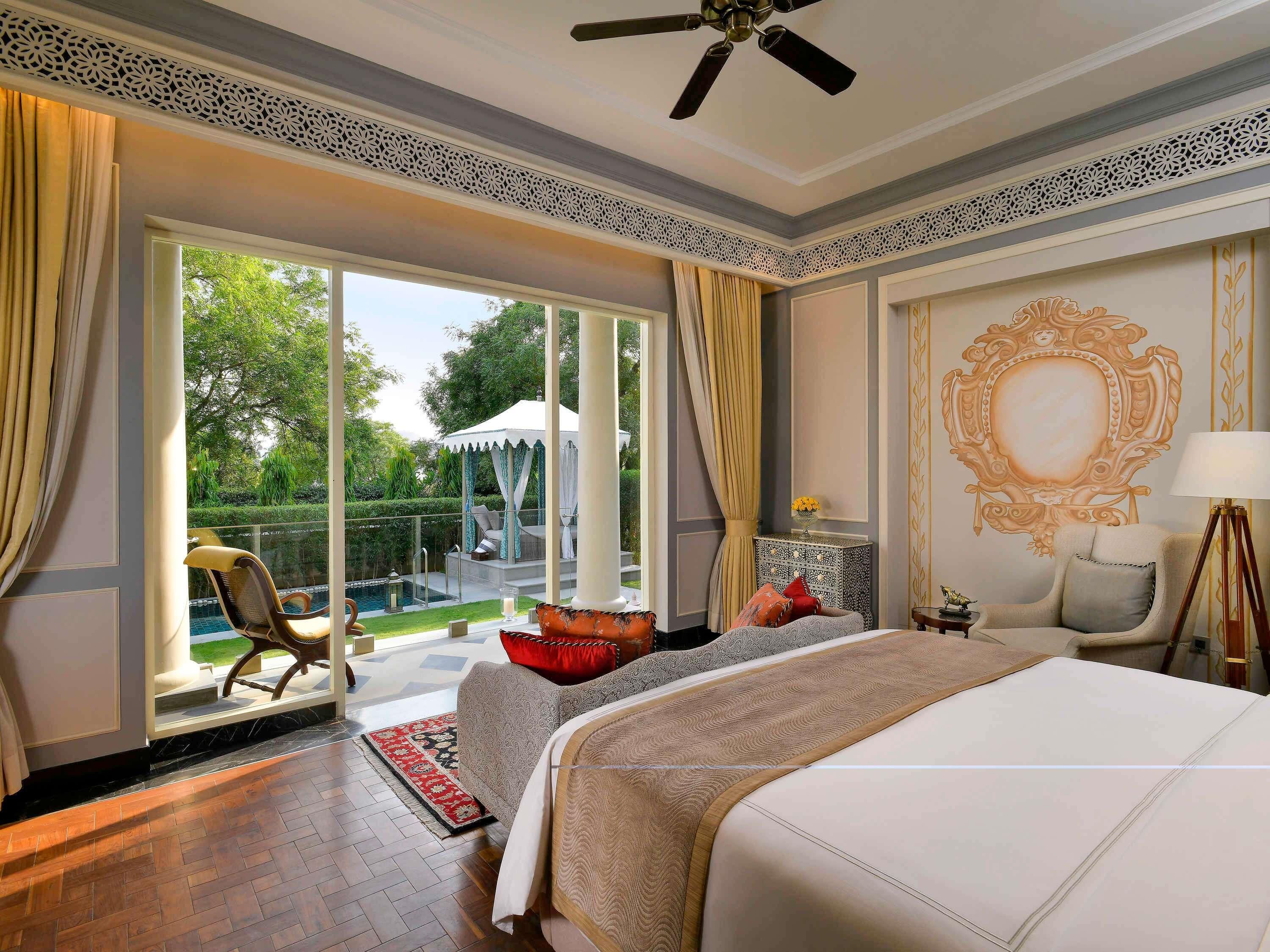 A bedroom with a bed, a chair, a lamp, and a view of a pool and garden.