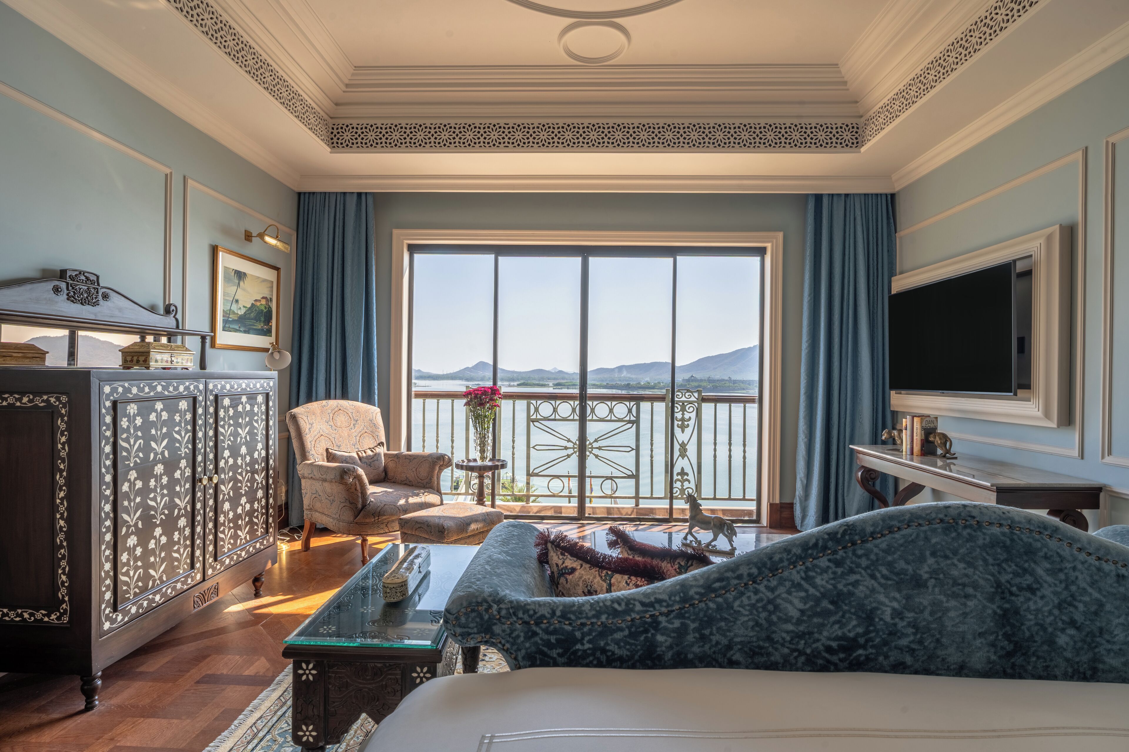 A spacious room with a large window, a sofa, a chair, a TV, and a cabinet.