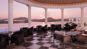 A covered outdoor seating area with checkered flooring, white columns, and wicker furniture. - Raffles Udaipur (Udaipur)