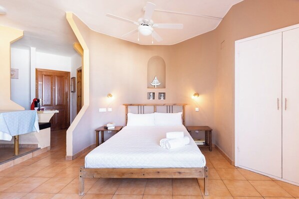 Une chambre à coucher comprenant un lit, des tables de chevet, une armoire, un ventilateur de plafond et une petite table avec une chaise.