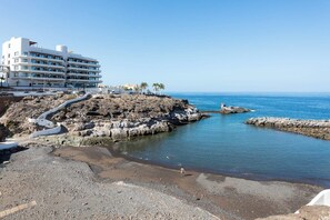Un hôtel situé sur la côte, avec un rivage rocheux, une mer d’un bleu limpide et une promenade pavée menant à la plage.