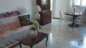 En stue med sofa, sofabord med vase, spisebord med stole og et skab.