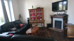 Una sala de estar con un sofá de cuero negro, una mesa de centro de madera, una vitrina con cristalería, una chimenea y un televisor montado en la pared.