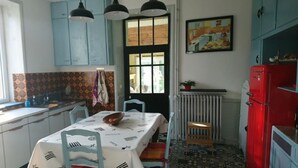 Una cocina con armarios azules, un refrigerador rojo, una mesa de comedor con sillas y una ventana con cortinas.