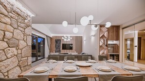 A modern dining area with a stone accent wall, a long wooden table set for six, and a contemporary chandelier. - Gorgeous Villa Luana with wellness and pool (Malinska)