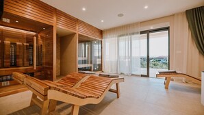 A modern spa room with wooden loungers, a glass-enclosed sauna, and a large sliding glass door leading to a balcony with a view. - Gorgeous Villa Luana with wellness and pool (Malinska)