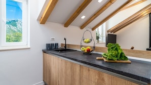 A modern kitchen with a black countertop, wooden cabinets, and a hanging fruit basket. - Stone villa Judita with heated pool and hydro-massage, Billiard Room (Makarska)
