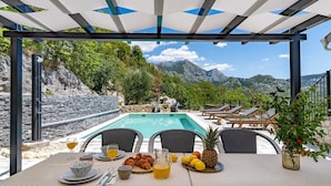 A poolside breakfast setup with a view of mountains. - Stone villa Judita with heated pool and hydro-massage, Billiard Room (Makarska)