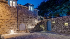 A stone building with a staircase leading to a second floor, a covered outdoor area with seating, and a view of a forested hillside. - Stone villa Judita with heated pool and hydro-massage, Billiard Room (Makarska)
