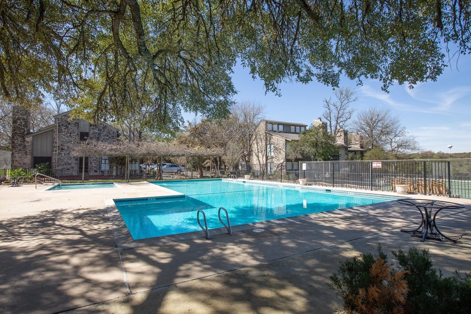 A swimming pool with two lanes, surrounded by a fenced area, stone buildings, and trees.