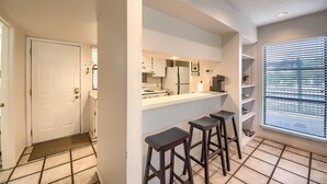 Una cocina moderna con encimera blanca, taburetes de bar y estanterías empotradas.