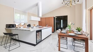 Una cocina moderna con una isla central, un comedor con mesa de madera y un ventanal grande que proporciona luz natural.