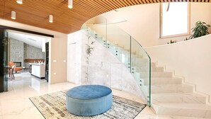 Un interior moderno con una escalera curva, un otoman redondo y una zona de cocina.