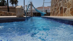 Una piscina con uno scivolo, un muro in pietra e acqua cristallina.