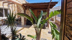 Una zona patio con pavimento in pietra, un pergolato in legno e diverse piante in vaso.