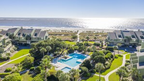 Un resort con piscina central rodeada de exuberante vegetación y vista al mar.