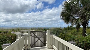 A wooden boardwalk leading to a gated entrance with a view of the beach and ocean.