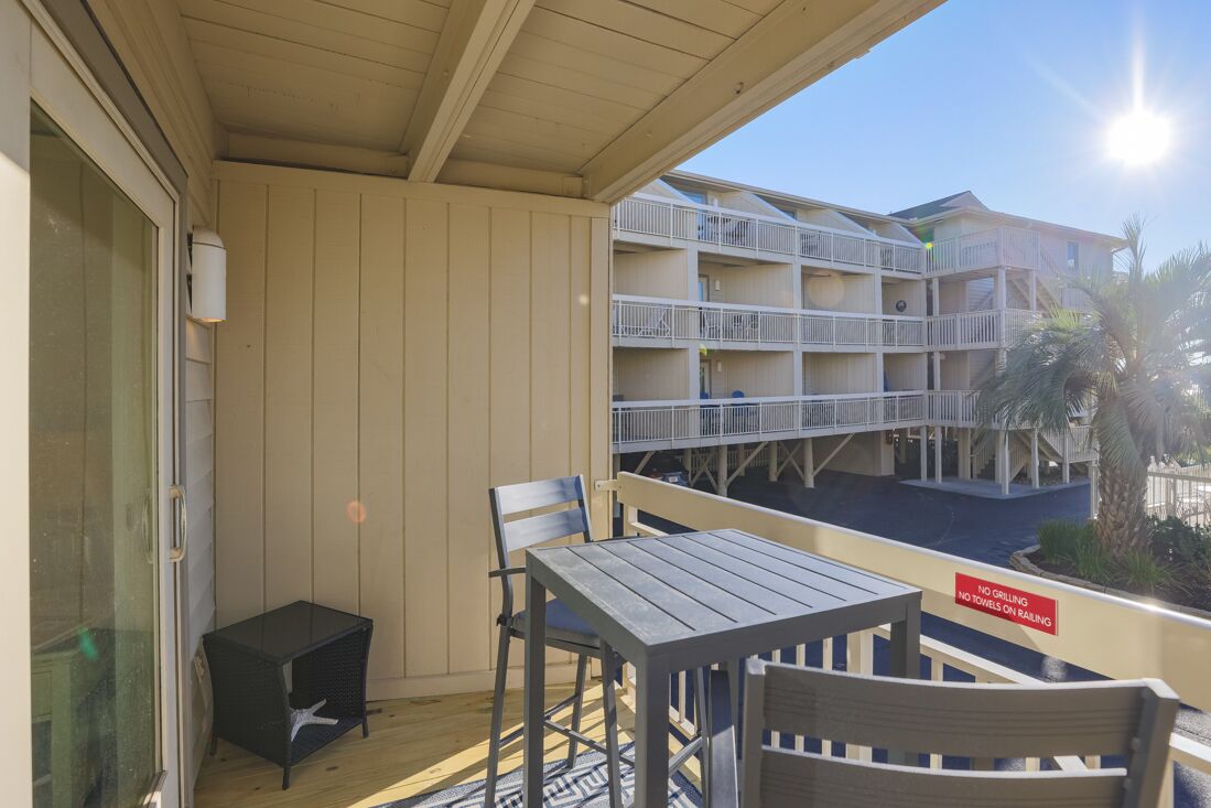 A balcony with a table and chairs, a small table, and a railing with a sign.