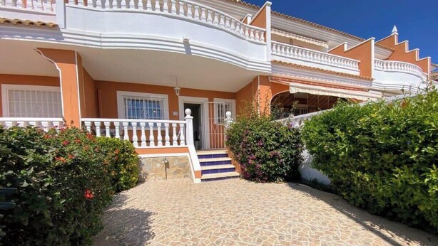 Uma casa de dois andares com varanda branca, porta de entrada e caminho de pedras.