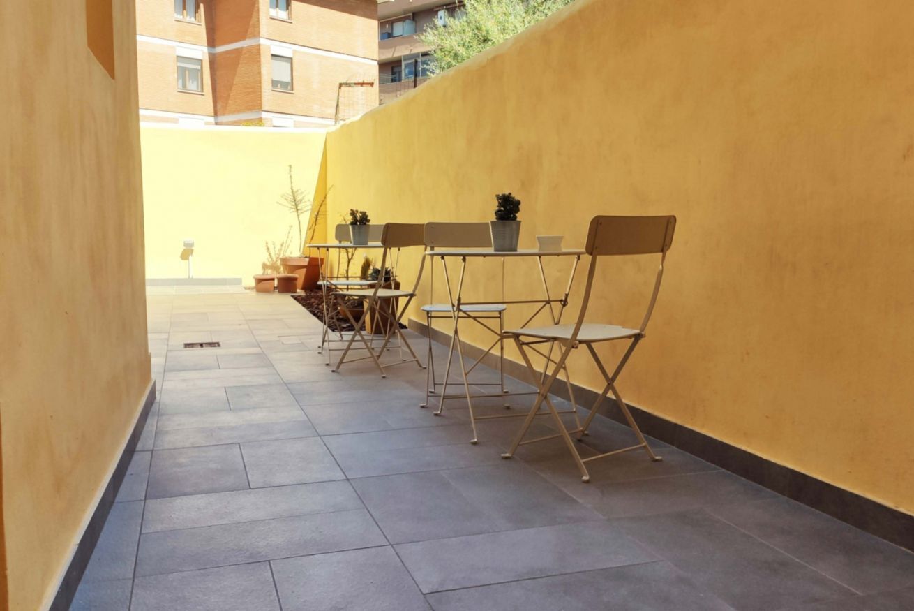 An outdoor seating area with foldable chairs and tables, potted plants, and a yellow wall.