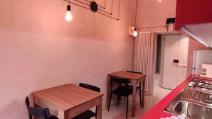 A compact kitchen with a red countertop, two wooden tables, and a modern pendant light fixture. - Lo Strullo - Ground Floor Suite (Pisa)