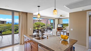 Una cocina moderna con una isla grande, un área de comedor con sillas y vistas a la ciudad a través de amplios ventanales.