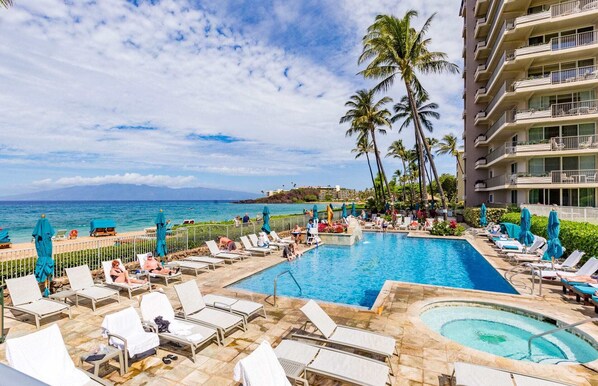 Relax by the oceanfront pool, surrounded by lounge chairs and umbrellas, with a hot tub nearby.