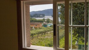 Vista pela janela, com vinhedo, um corpo d'água e colinas ao longe.