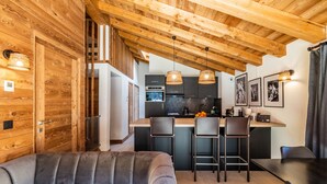 A modern kitchen with wooden beams, a sofa, and a dining area. - SAPELLI - Design apartment in brand-new residency (Chamonix-Mont-Blanc)