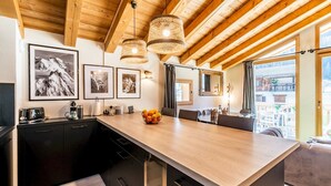 A modern kitchen with a wooden island, black cabinets, and a dining area with a view. - SAPELLI - Design apartment in brand-new residency (Chamonix-Mont-Blanc)