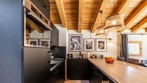 A modern kitchen with wooden beams, a long counter, and framed mountain photographs. - SAPELLI - Design apartment in brand-new residency (Chamonix-Mont-Blanc)