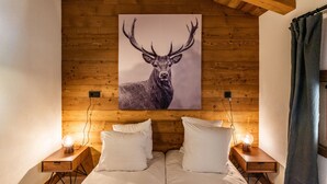 A bedroom with a wooden ceiling, a large deer painting on the wall, two bedside tables with lamps, and a bed with white bedding. - SAPELLI - Design apartment in brand-new residency (Chamonix-Mont-Blanc)