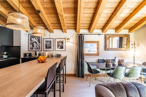 Une cuisine moderne avec des poutres en bois, un coin repas avec une table et des chaises en bois, et un grand miroir.