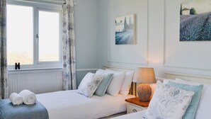 A bedroom with two beds, a window with curtains, and a lamp on a bedside table. - Great sea views, close to a small beach and Flamborough Head lighthouse. (Flamborough)