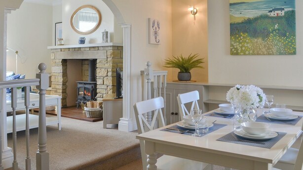 A dining area with a stone fireplace, white furniture, and a painting of a coastal scene. - Great sea views, close to a small beach and Flamborough Head lighthouse. (Flamborough)