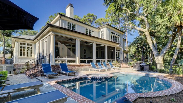Une maison avec une piscine, un espace salon extérieur et une véranda.