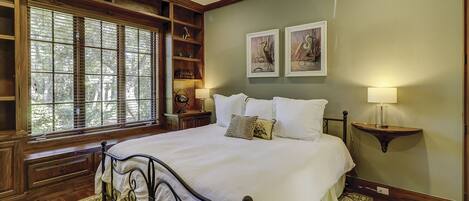 A bedroom with a large bed, wooden headboard, built-in shelving, and a window with blinds.