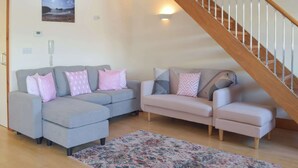 Ein Wohnzimmer mit zwei Sofas, einem gemusterten Teppich, einer Holztreppe und einer wandmontierten Leuchte.